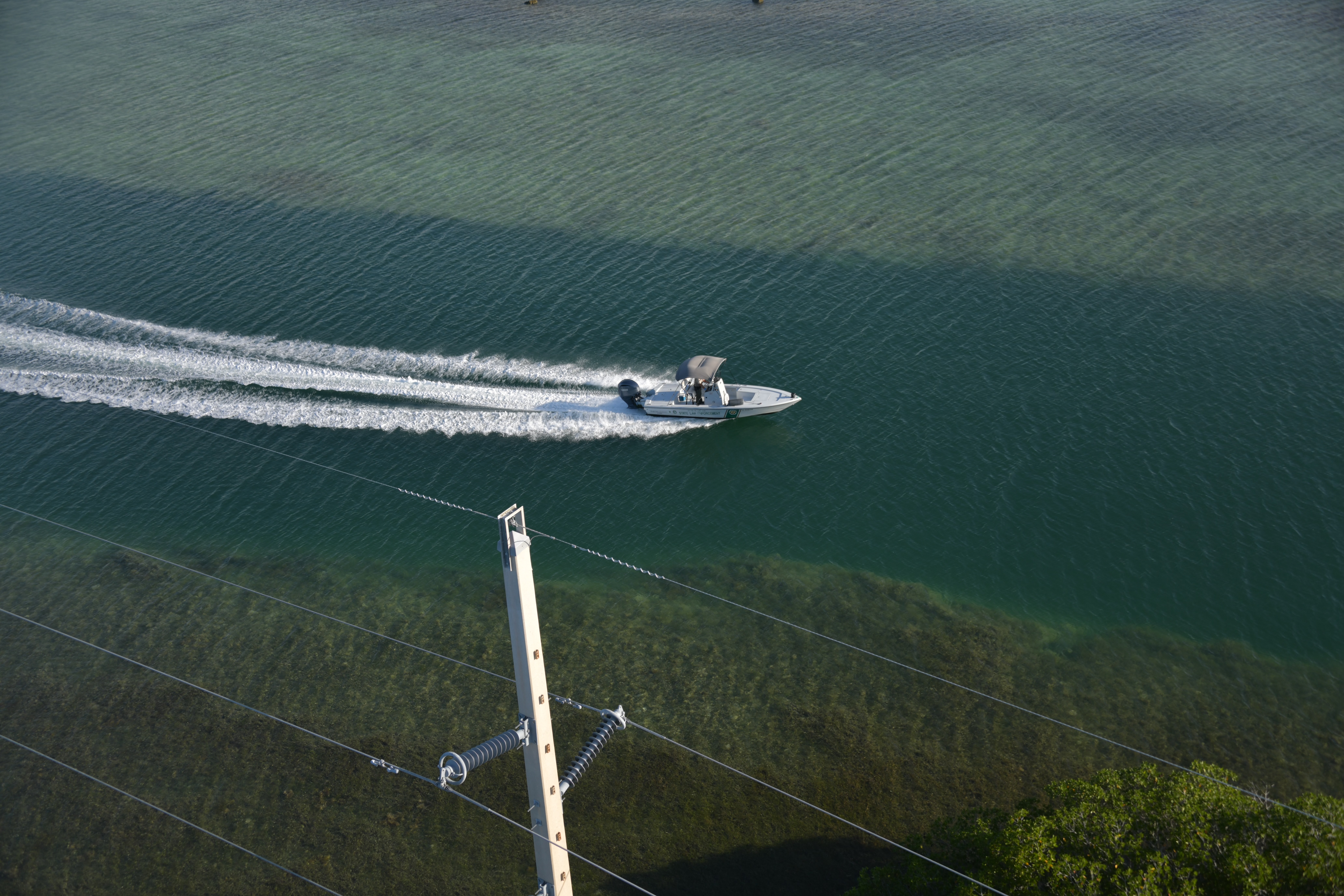Aerial view of a state law enforcement vessel underway in the Florida Keys, with shoreline infrastructure in the foreground.